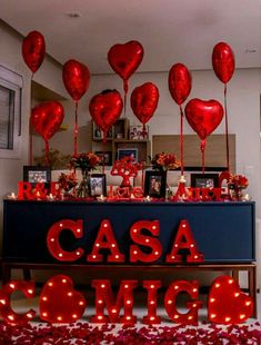 a table topped with lots of red heart shaped balloons next to a sign that says casa comics