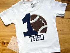 Happy 1st Birthday!! Celebrate a little boy's first birthday with this embroidered football birthday shirt! This high quality shirt is custom made by me and can be personalized with the special birthday boy's name. Please message me if you would like a different fabric/thread color for the name!  Choose between a short sleeve or long sleeve tee.  This shirts are true to size and 6.5-6.7 oz 100% combed cotton.  Turnaround time is 7 business days to ship to you. This does NOT include the amount of time it will take to ship to you. Please keep this in mind when ordering.  I do not accept returns on these items, as they are custom made for each order. Thank you so much for shopping small! First Birthday Boy Shirt, Football Birthday Shirt, 1st Year Down Football Birthday Shirts, Football One Year Old Birthday Shirt, Customizable Fitted T-shirt For First Birthday, 1st Birthday Shirts, First Birthday Shirts, Football Birthday, Birthday Boy Shirts