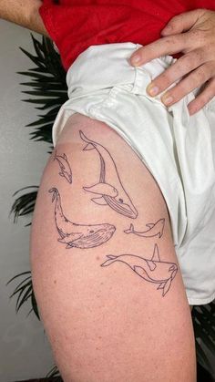 a woman with a tattoo on her thigh showing dolphins swimming in the water and jumping up into the air