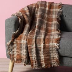 a couch with a plaid blanket on it next to a wooden floor and pink wall