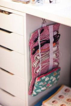 a purse hanging on a wall next to a white dresser with books and magazines in it