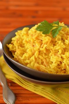 a bowl filled with yellow rice and garnished with parsley on the side