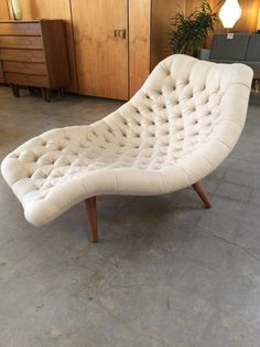 a white chaise lounge chair sitting on top of a floor next to a wooden cabinet