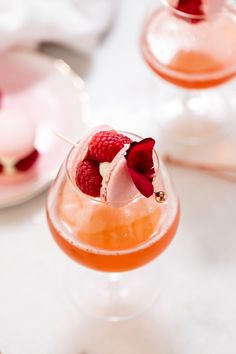 two glasses filled with drinks and garnished with raspberries on a table