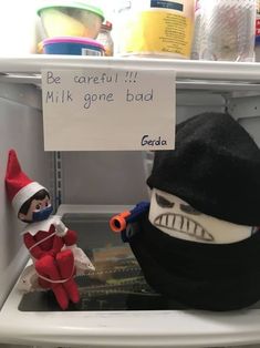 two elf dolls sitting on top of an open refrigerator with a sign that says be careful milk gone bad