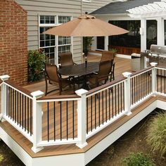 a deck with an umbrella over it next to a grill and patio furniture on the other side