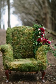 an old chair covered in moss and flowers