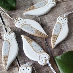 four ceramic owl ornaments hanging from strings on a wooden table with green leaves and greenery