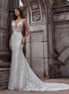 a woman in a white wedding dress standing by an old stone archway with her hands on her hips