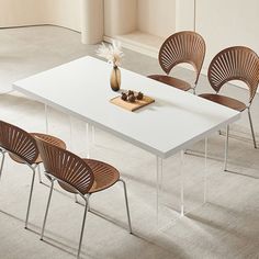 a white table with four chairs and a vase on the top, in an empty room