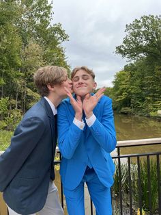 two young men in blue suits standing next to each other with their hands on their mouths