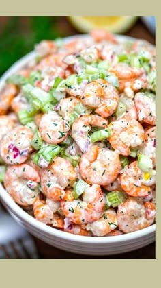 a bowl filled with shrimp and celery on top of a table next to a fork