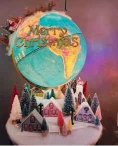 a christmas globe on top of a table with houses and trees in the foreground