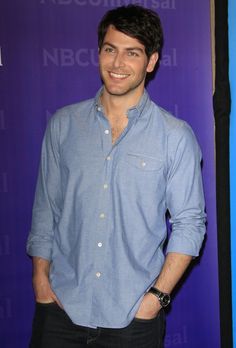 a man standing in front of a purple wall with his hands in his pockets and smiling