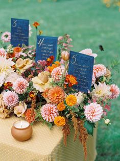 an arrangement of flowers and candles on a table with two blue cards in the center