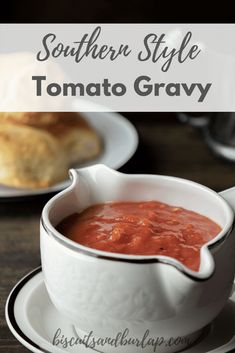 a white bowl filled with tomato sauce on top of a wooden table next to bread