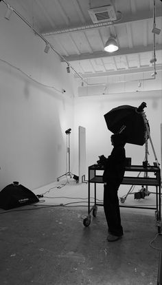 black and white photograph of photographer setting up his equipment in an empty room with lights on the ceiling