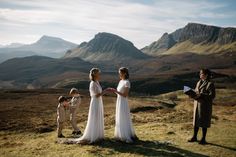 a couple of people standing on top of a grass covered field with mountains in the background