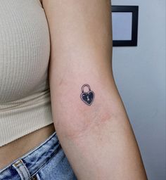 a woman's arm with a small heart shaped lock tattoo on the left shoulder