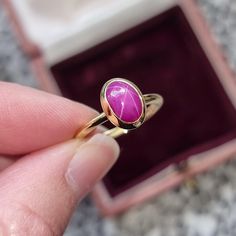 A stunning yet modest ring from he early 2000's, the head featuring an oval shaped, cabochon cut star ruby, bezel set and mounted on a plain shank, all in 18ct yellow gold. What is a star ruby? From Wikipedia: An asterism (from Ancient Greek ἀστήρ (astḗr) 'star' and -ism) is a star-shaped concentration of light reflected or refracted from a gemstone. It can appear when a suitable stone is cut en cabochon (i.e. shaped and polished, not faceted).  It occurs in rubies, sapphires, garnet, diopside, Yellow Gold Ruby Ring With Oval Cabochon, Oval Cabochon Ruby Ring In Yellow Gold, Vintage Hallmarked Ruby Ring With Oval Cabochon, Red Ruby Oval Cabochon Ring In 14k Gold, Classic Red Ruby Ring, Oval Cabochon, Ruby Solitaire Ring, Spinel Ring, Star Sapphire, Star Ruby