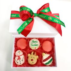 four decorated cookies in a white box with red ribbon