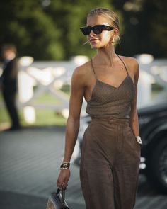 a woman walking down the street with sunglasses on her head and a handbag in her other hand