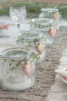 some glass jars with plants in them sitting on a cloth tablecloth and place settings