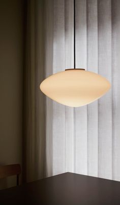 a white light hanging over a table in front of a curtained window with sheer drapes