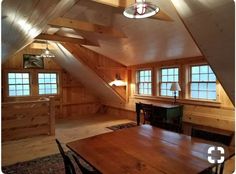 an attic with wood paneling and wooden table in the center, surrounded by two windows