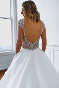 a woman in a white wedding dress looking down at her back and wearing a beaded top