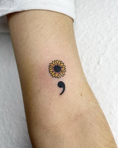 a small sunflower tattoo on the left inner arm, with a black hook in the middle