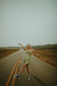 a woman is dancing on the side of an empty road with her arms outstretched in the air