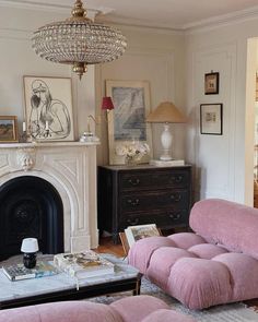 a living room with pink couches and a chandelier above the fire place