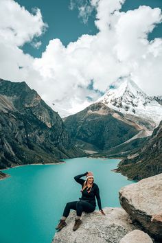 a woman sitting on top of a large rock next to a lake in the mountains