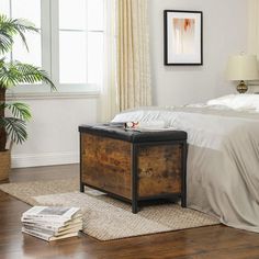 a bedroom with white walls and wood flooring has a wooden trunk on the bed