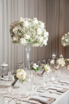 the table is set with silverware and white flowers in tall vases on each side