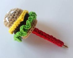 a crocheted lollypop with a hamburger on it's end, sitting on a white surface