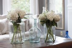 three vases filled with white flowers sitting on top of a table next to a couch