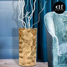 a gold vase with branches in it sitting next to a blue chair and curtained window