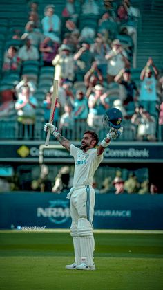 a man holding a cricket bat on top of a field in front of a crowd