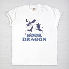 Immerse yourself into a fantasy world with our Book Dragon Comfort Colors T-Shirt. Blend your passion for dragons and love for books with this comfy cotton tee. The design features a stylish 'Book Dragon' catchphrase that echoes your identity as a fantasy reader in a fun way. This T-shirt is made from 100% ringspun cotton, offering a vintage feel and ultimate comfort, making it your perfect companion for reading marathons or casual day outs. Each book dragon shirt is lovingly crafted, promising longevity and consistent comfort. Stand out and wear your love for books and dragons with this unique shirt! Experience cozy reading bliss every day in a Comfort Colors 1717 unisex tee. Revel in the luxurious feel of 100% USA grown, ring-spun cotton and enjoy a garment that's been washed to peak sof Literary Crew Neck T-shirt With Screen Print, Bookish Cotton T-shirt With Slogan, Screen Print Crew Neck T-shirt, Literary Graphic Print Crew Neck T-shirt, Literary Cotton T-shirt With Text Print, Cotton Bookish Slogan T-shirt, Book Dragon Shirt, Romantasy Books, Best Fantasy Series