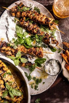 grilled chicken skewers on a platter with dips and parsley