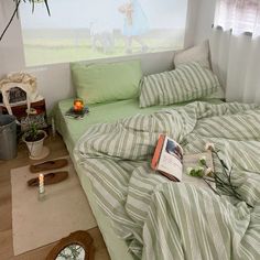 an unmade bed with green and white striped sheets in a bedroom next to a potted plant