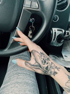 a woman's hand on the steering wheel of a car, with tattoos on her arm