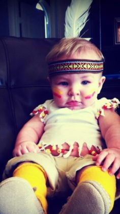 a baby sitting on top of a chair wearing yellow socks and a feather headband