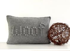 a crocheted pillow sitting on top of a white shelf next to a ball of yarn