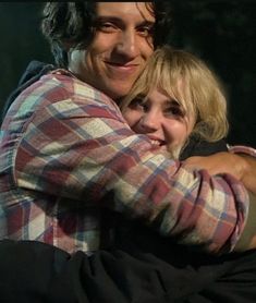 two people hugging each other in front of a dark background and one person has his arms around the other