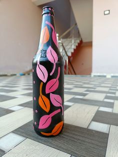 a black bottle with pink and orange designs on it sitting on a checkered floor