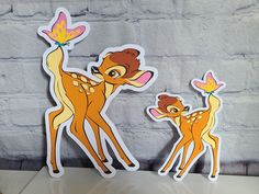 two deer stickers sitting next to each other on top of a table in front of a brick wall