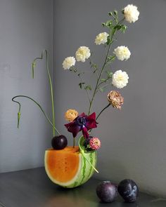 an arrangement of flowers and fruit in a vase